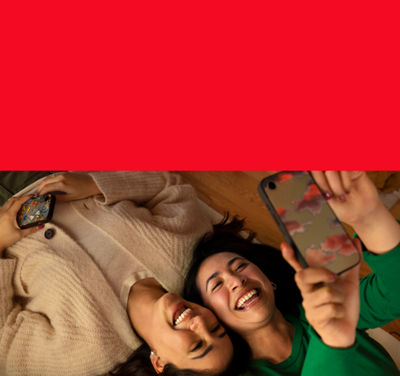 Two women lying on the floor, looking at one of their phones