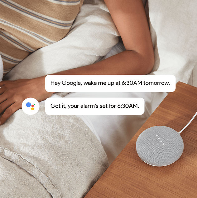 Google Home Mini with comment bubbles floating above – indicating conversation. 'Hey Google, wake me up at 6:30AM tomorrow.'  'Got it, your alarm’s set for 6:30AM.'