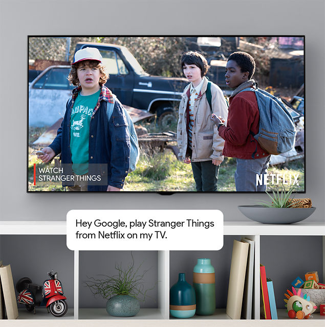 Flat screen TV mounted on wall with in modern living room. Scene from Netflix Stranger Things on screen. Commentary bubble 'Hey Google, play Stranger Things from Netflix on my TV.'