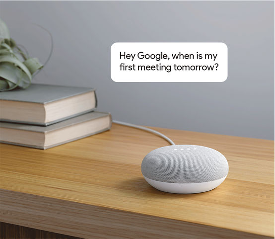 Google Home Mini with comment bubble floating above – 'Hey Google, when is my first meeting tomorrow?'