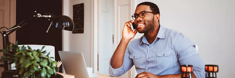 Man with a phone and internet bundle uses his smartphone in his brightly colored home office.