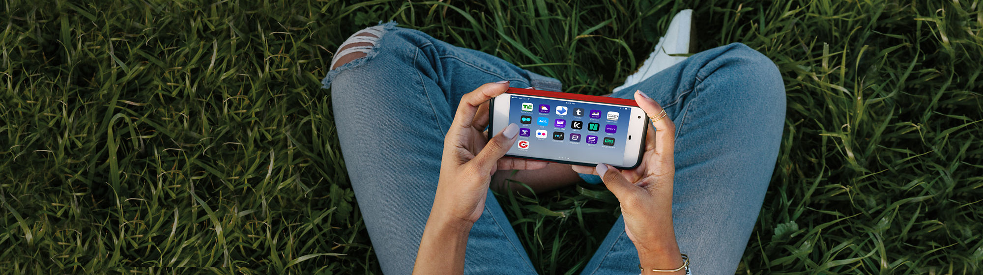 First person view of person sitting with legs crossed in the grass, viewing home screen of mobile phone